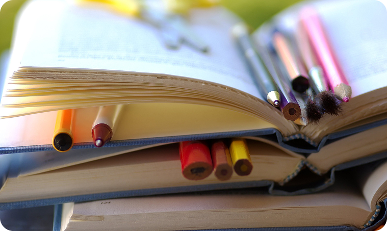 Open books stacked with colored pencils between the pages