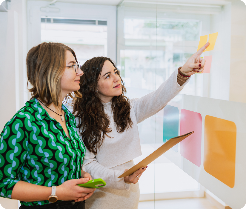 Two people arranging sticky notes on a glass board